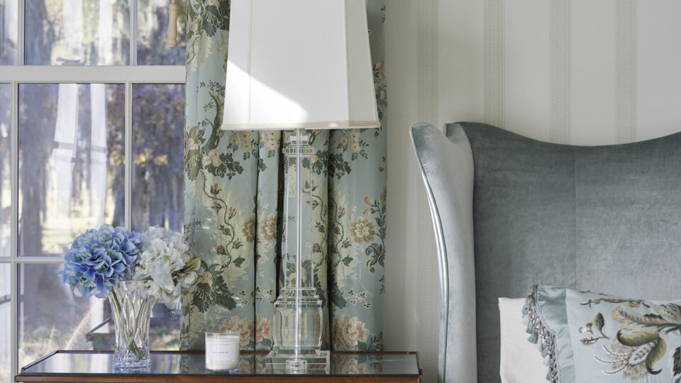 Charming bedroom interior featuring floral curtains, a wooden nightstand, and a cozy bed with decora.