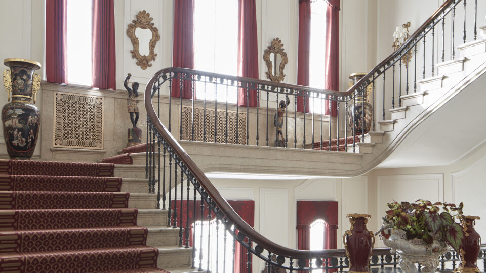 Armstrong Kessler staircase with ornate iron railing and rich red carpet.