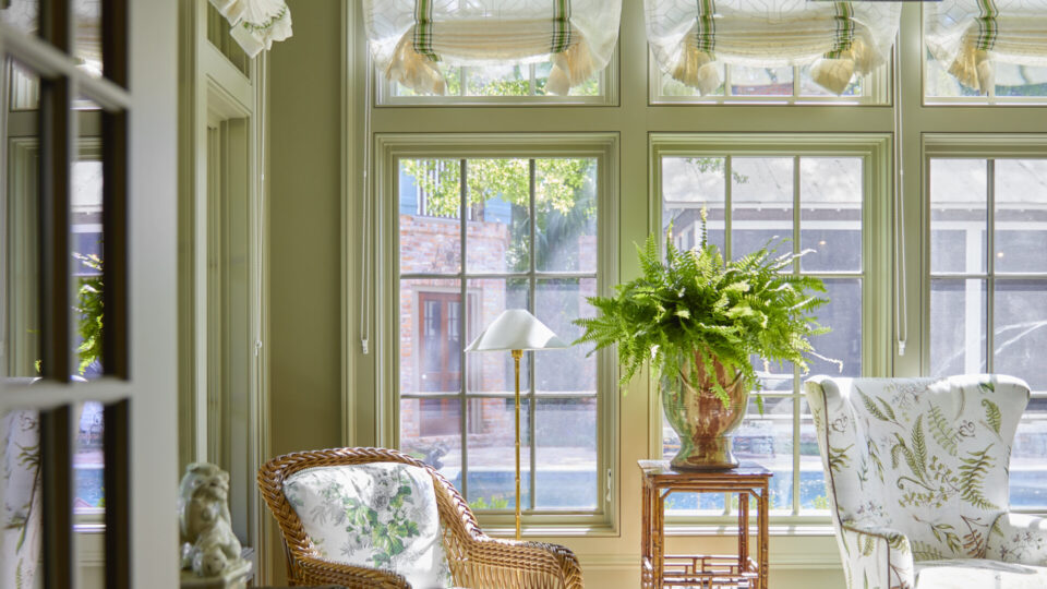 An inviting sunroom featuring wicker and upholstered chairs, lush greenery, and large windows for na.